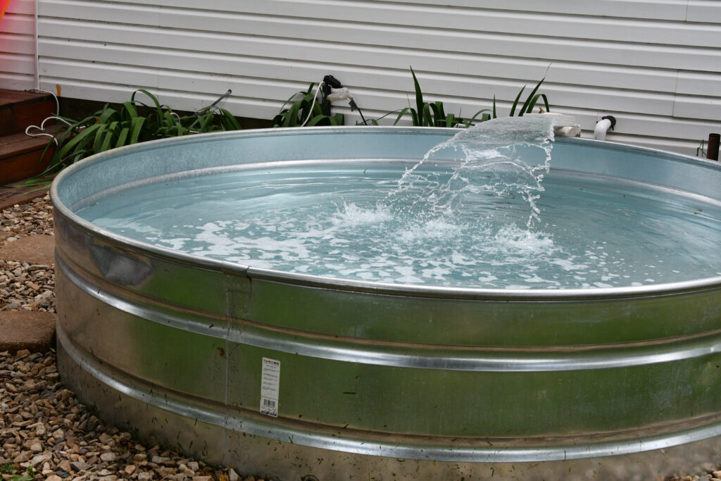 Galvanized stock tank pool with running water in backyard requiring proper electrical power setup for pump and filtration equipment